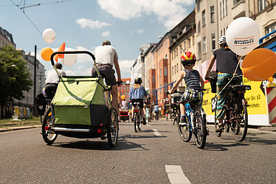 Familie auf Rändern mit Fahrradanhänger auf städtischer Straße von hinten zu sehen