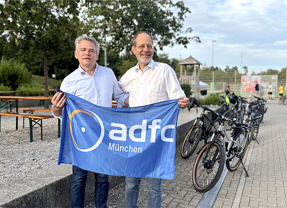 zwei Männer lächelnd mit ADFC München Fahne neben Fahrrädern