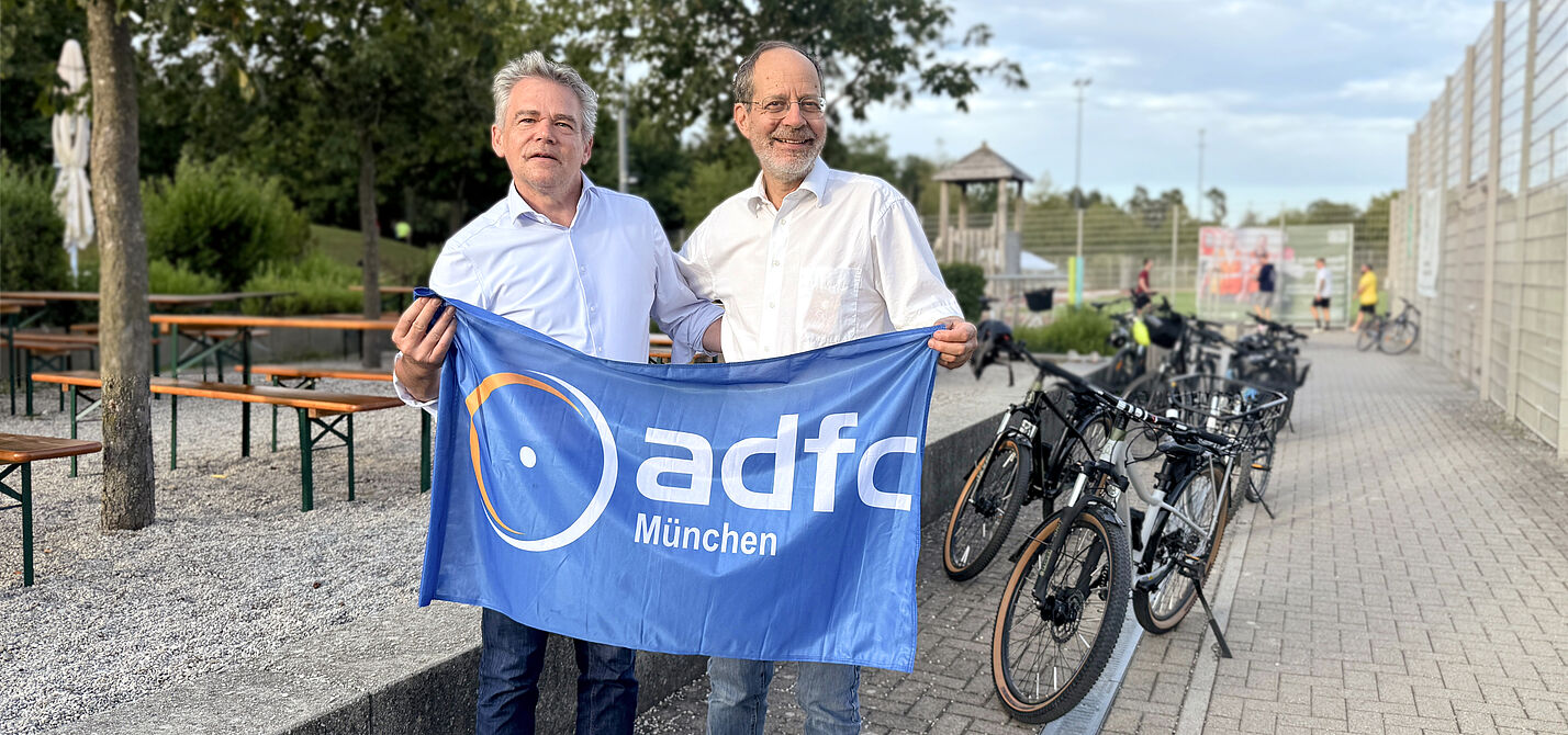 zwei Männer lächelnd mit ADFC München Fahne neben Fahrrädern