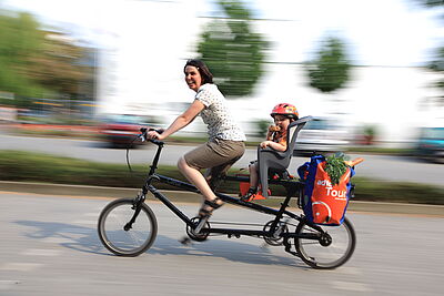 Frau mit Kind und Einkauf auf Lastenrad