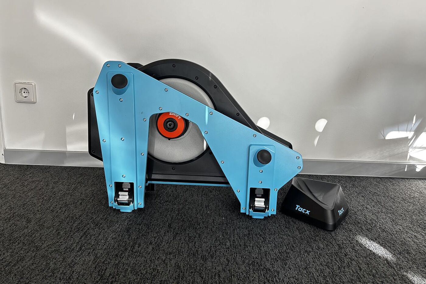 Ein Smarttrainer mit eingeklappten Beinen steht vor einer weißen Wand. 
